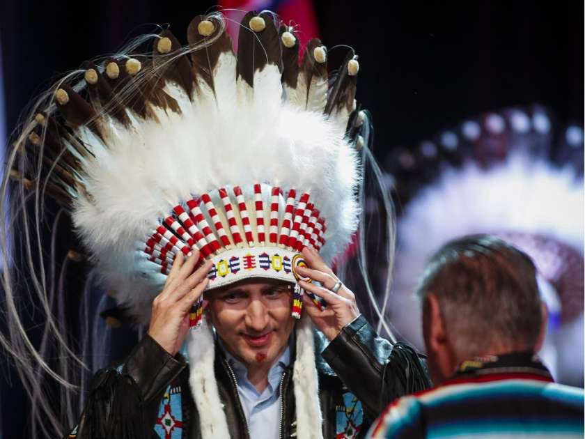 Prime Minister Justin Trudeau, left, adjusts his new headdress as Tom Heavenfire looks on during a ceremony while visiting the Tsuu T'ina First Nation near Calgary, Alta., Friday, March 4, 2016.THE CANADIAN PRESS/Jeff McIntosh